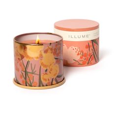 a candle that is sitting in front of a box with flowers on it's lid