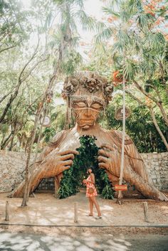 a woman standing in front of a giant wooden statue that looks like a human face