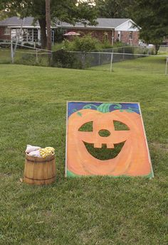 a pumpkin shaped sign sitting on top of a lush green field next to a barrel