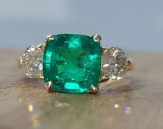 an emerald and diamond ring sitting on top of a table