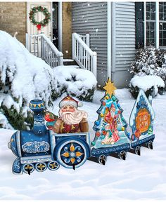 a christmas train with santa claus and other decorations in front of a house on a snowy day