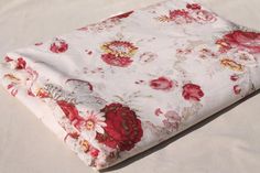 a white and red flowered blanket laying on top of a bed