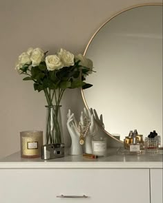 a white dresser topped with lots of flowers and candles next to a large round mirror