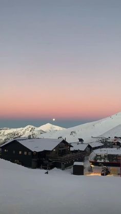 the sun is setting over a snowy mountain with houses and mountains in the background at dusk