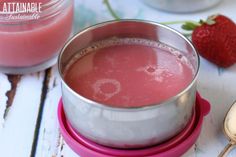 there is a pink liquid in a metal cup next to strawberries and spoons