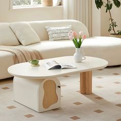 a living room with a white couch and coffee table in front of a potted plant