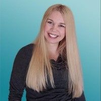 a woman with long blonde hair smiling at the camera and wearing a black shirt, standing in front of a blue background