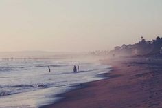 some people are walking on the beach in the water and foggy weather is coming