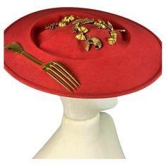 Circa 1980 France A stunning scarlet wool felt Hat Capeline with Surrealist inspiration by French designer Isabel Canovas dating from the 1980s. Entitled déjeuner au Stresa (lunch in Stresa), this capeline is shaped like an oval plate filled with various charms and a gilded bronze fork on one edge! A wide black elastic band and headband behind the bun or the nape of the neck reveals the Isabelle Canovas label. Very slight creasing of the base plate resting on the skull, otherwise no other defect 1980’s Fashion, Oval Plate, Antique Hats, Oval Plates, French Designer, Red Felt, The 1980s, Felt Hat, Luxury Accessories