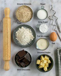 ingredients for chocolate cake laid out on a marble counter top with rolling pin, measuring spoons and flour