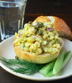 an egg salad on a bagel bun with celery next to a glass of water