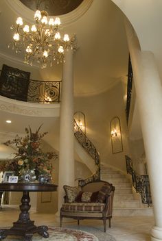 a living room filled with furniture and a chandelier hanging from the top of a spiral staircase