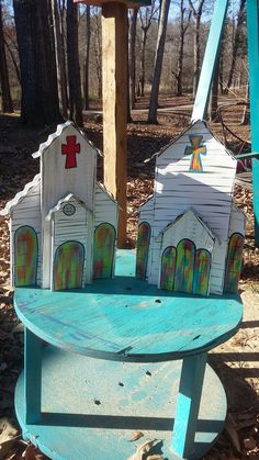 a bench made out of wood with houses painted on the top and bottom, sitting in front of a cross