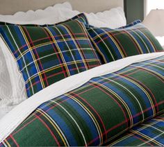 a plaid comforter and pillows on a bed with two lamps in the corner behind them