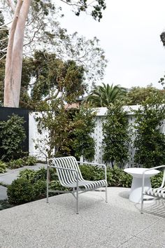 two white chairs sitting next to each other on top of a cement floor covered patio