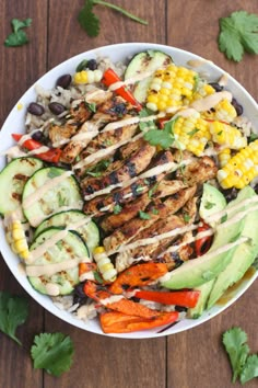 a white bowl filled with grilled chicken, vegetables and dressing on top of a wooden table