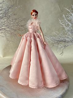 a doll in a pink dress standing on a table