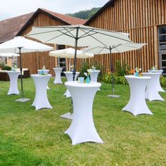 tables and umbrellas are set up outside on the grass in front of a barn