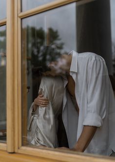 a man and woman standing next to each other in front of a window looking out at the street