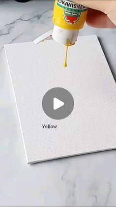 a person is using yellow paint on a white piece of paper with the word below it