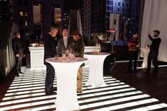 several people are standing around a table with wine glasses on it in the middle of a city at night