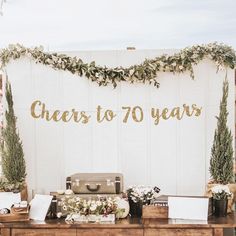 a wooden table topped with lots of flowers next to a sign that says cheers to 80 years