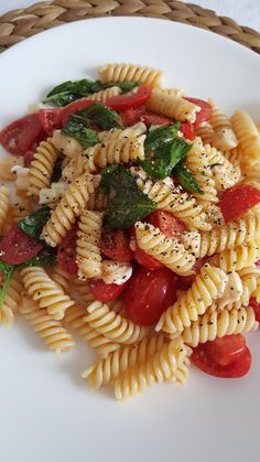 pasta with tomatoes, spinach and cheese on a white plate next to a woven basket