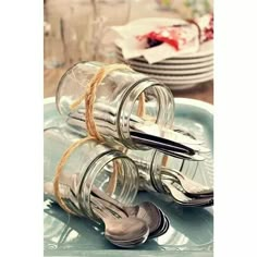 two glass jars with spoons and forks tied to each other on a blue plate