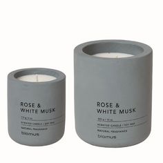 two white candles sitting next to each other on top of a wooden table with the words rose and white musk written in black