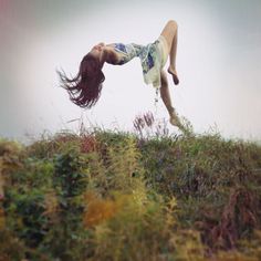 a woman is doing a handstand on top of a grassy hill with her hair blowing in the wind