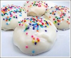 three white frosted donuts with sprinkles on them sitting on a wooden surface