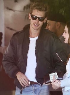 a man in sunglasses and a white t - shirt is talking to a woman wearing jeans