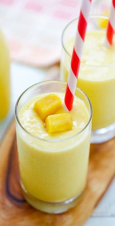 two glasses filled with yellow smoothie on top of a cutting board