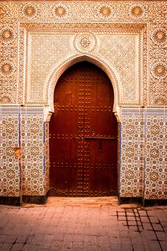 an ornate doorway with blue and white tiles on the outside, leading to a red door