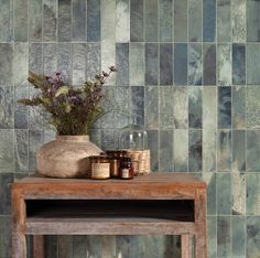 a wooden table topped with a vase filled with flowers next to a wall covered in tiles