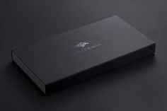 an open black box on a dark surface with the lid closed and logo printed on it