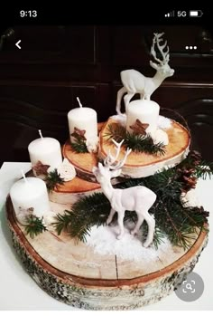 there are candles and deer figurines on top of a tree stump with pine needles