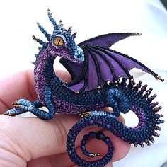 a purple dragon brooch sitting on top of a person's finger