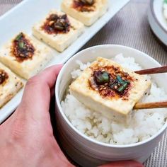 someone is holding chopsticks over rice in a bowl with tofu on it