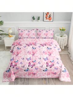 a bed with pink butterflies on it in a room next to a white table and potted plant