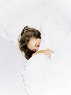 a woman is laying in bed with her head on the pillow and looking at the camera