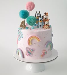 there is a cake decorated with animals and rainbows on the top, along with pom poms