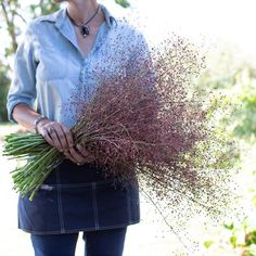 a woman holding a bunch of purple flowers in her hands and looking at the camera