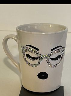 a white coffee cup with a face painted on the side and some jewels around it