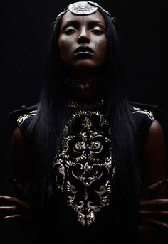 a woman with black hair and gold make - up on her face is standing in front of a dark background