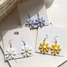 three pairs of earrings with yellow and blue flowers hanging from the earwires on top of each other