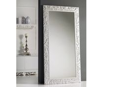 a large white mirror sitting on top of a floor next to a shelf filled with candles