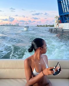 a woman is sitting on the back of a boat in the water while holding a remote control