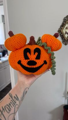 a hand holding an orange crocheted pumpkin with ears and horns on it's head