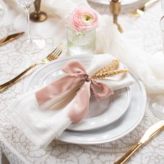 the table is set with white plates, silverware and pink flowers in vases